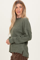 woman wearing a dark green oversized ribbed sweater with side slits and long sleeves