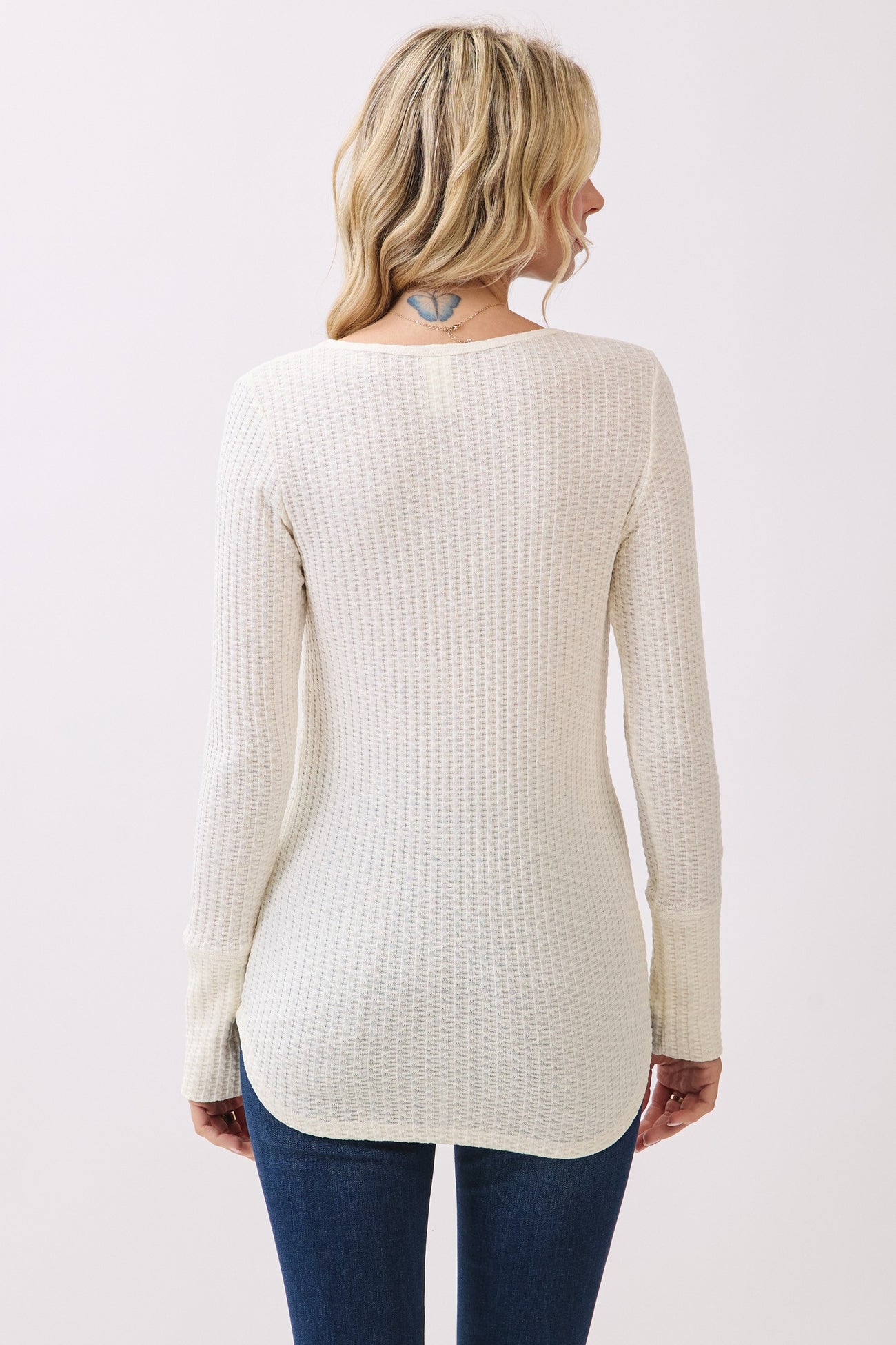 woman wearing a cream ribbed long sleeve top with a rounded hem and back detail, paired with blue jeans