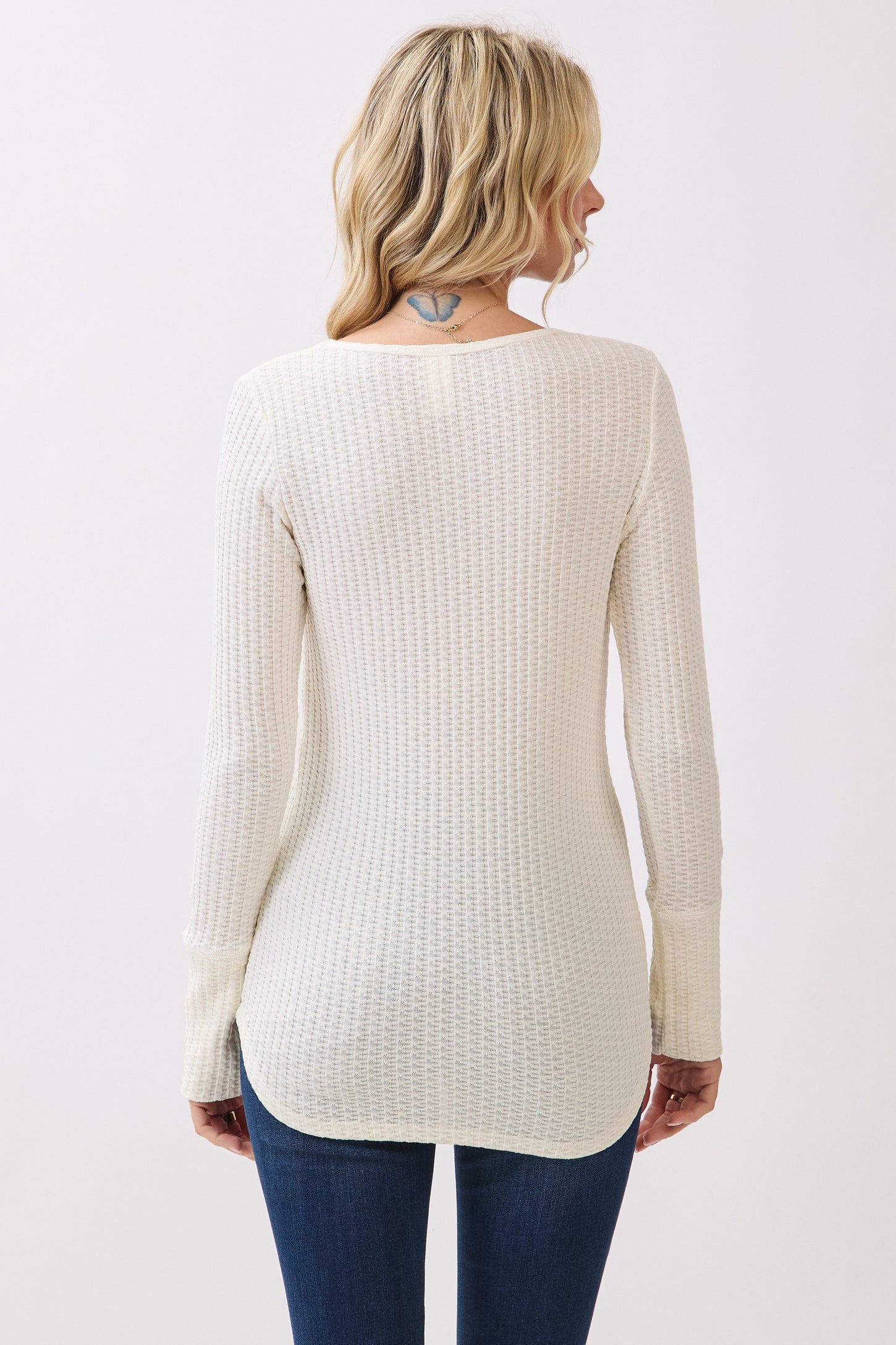 woman wearing a cream ribbed long sleeve top with a rounded hem and back detail, paired with blue jeans