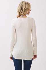 woman wearing a cream ribbed long sleeve top with a rounded hem and back detail, paired with blue jeans