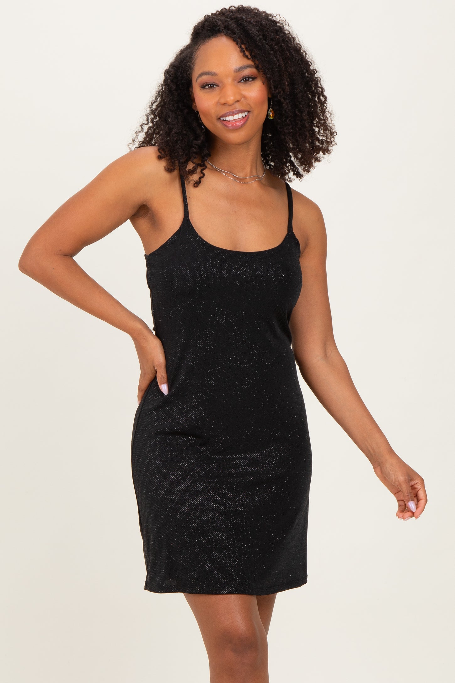 woman wearing a black sparkly mini dress with thin straps and a relaxed fit, smiling at the camera