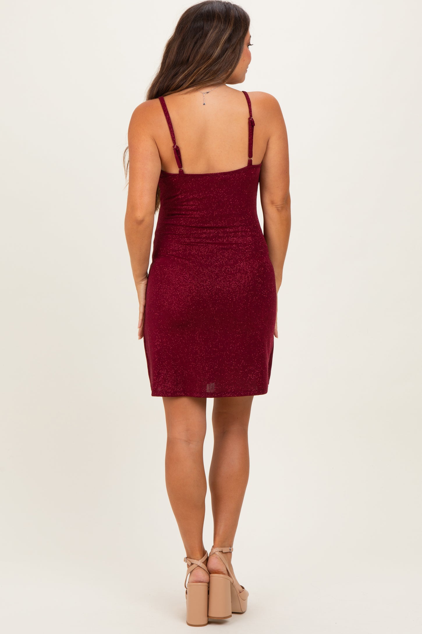 woman wearing a burgundy sparkly maternity dress with adjustable straps, showing a fitted silhouette from the back