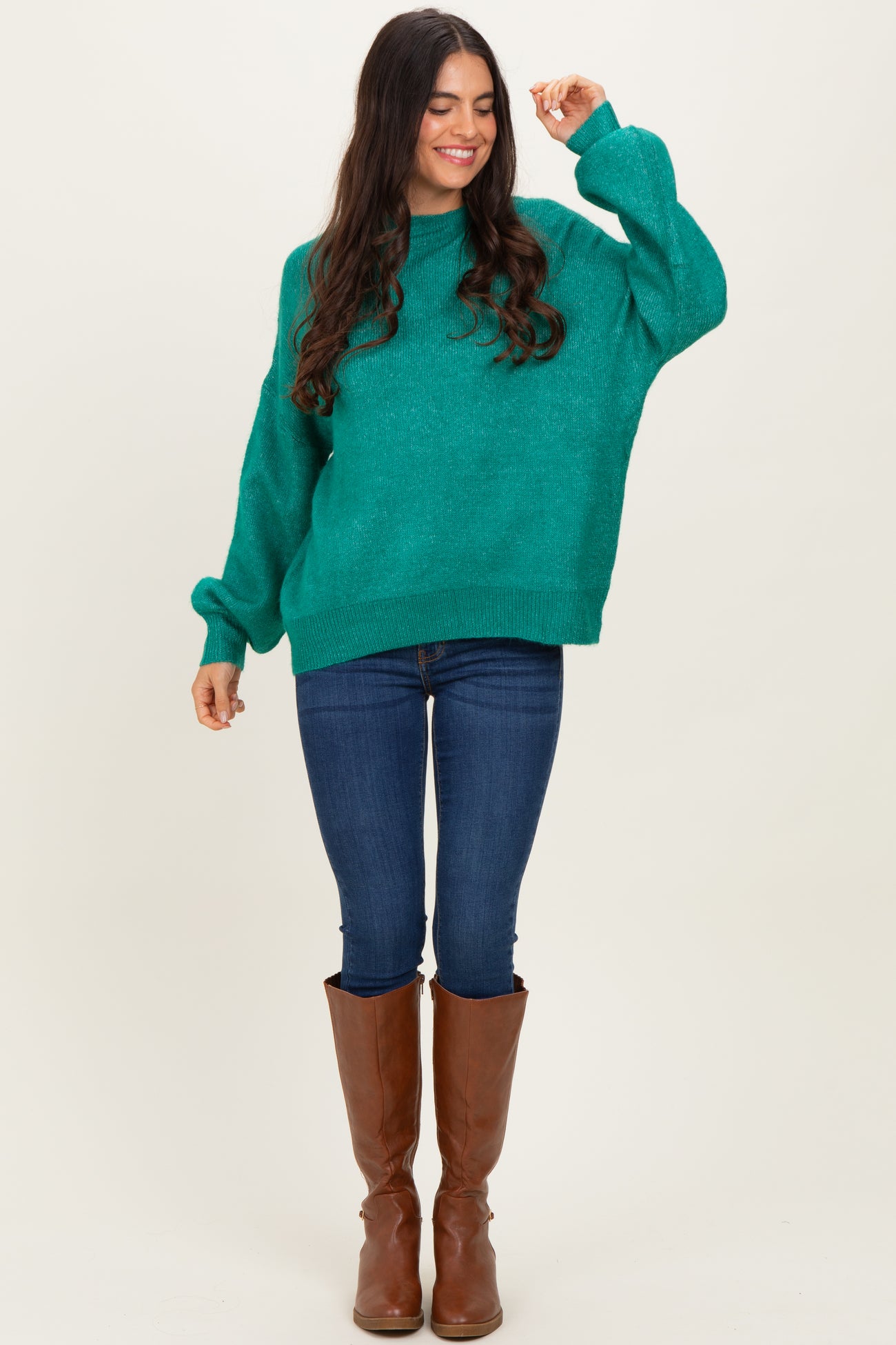 woman wearing a teal oversized sweater and fitted jeans, paired with knee-high brown boots