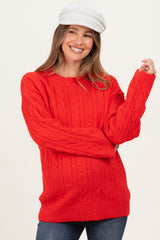 woman wearing a bright red cable knit maternity sweater with a relaxed fit and long sleeves