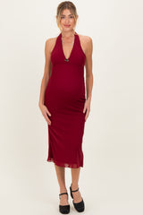 woman wearing a burgundy halter neck maternity dress with a fitted silhouette and a baby bump visible