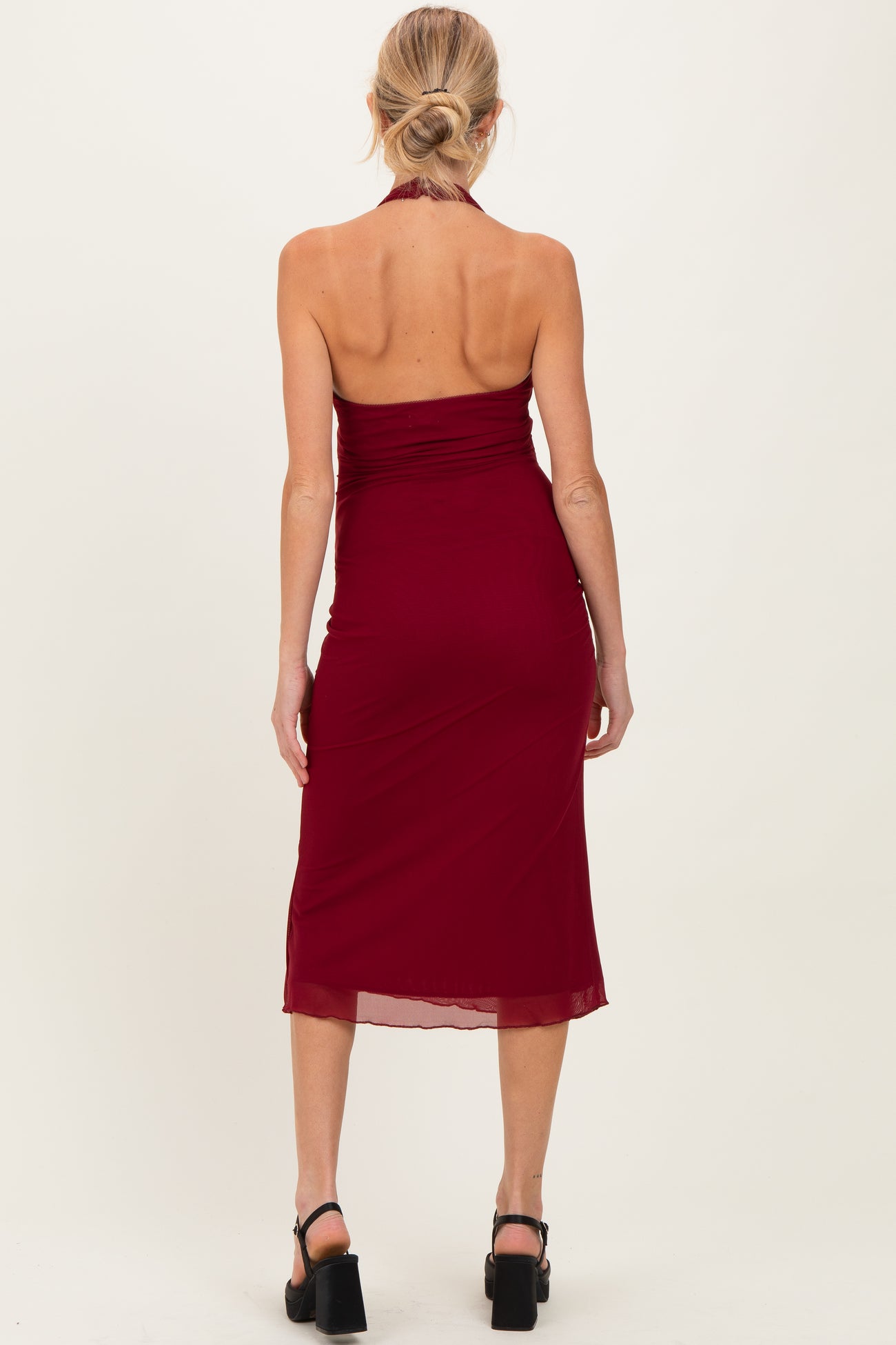 woman wearing a burgundy maternity halter neck dress with ruched details, showing a fitted silhouette from the back