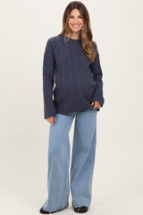 woman wearing a dark blue cable knit maternity sweater with loose fit paired with light blue wide leg jeans and smiling