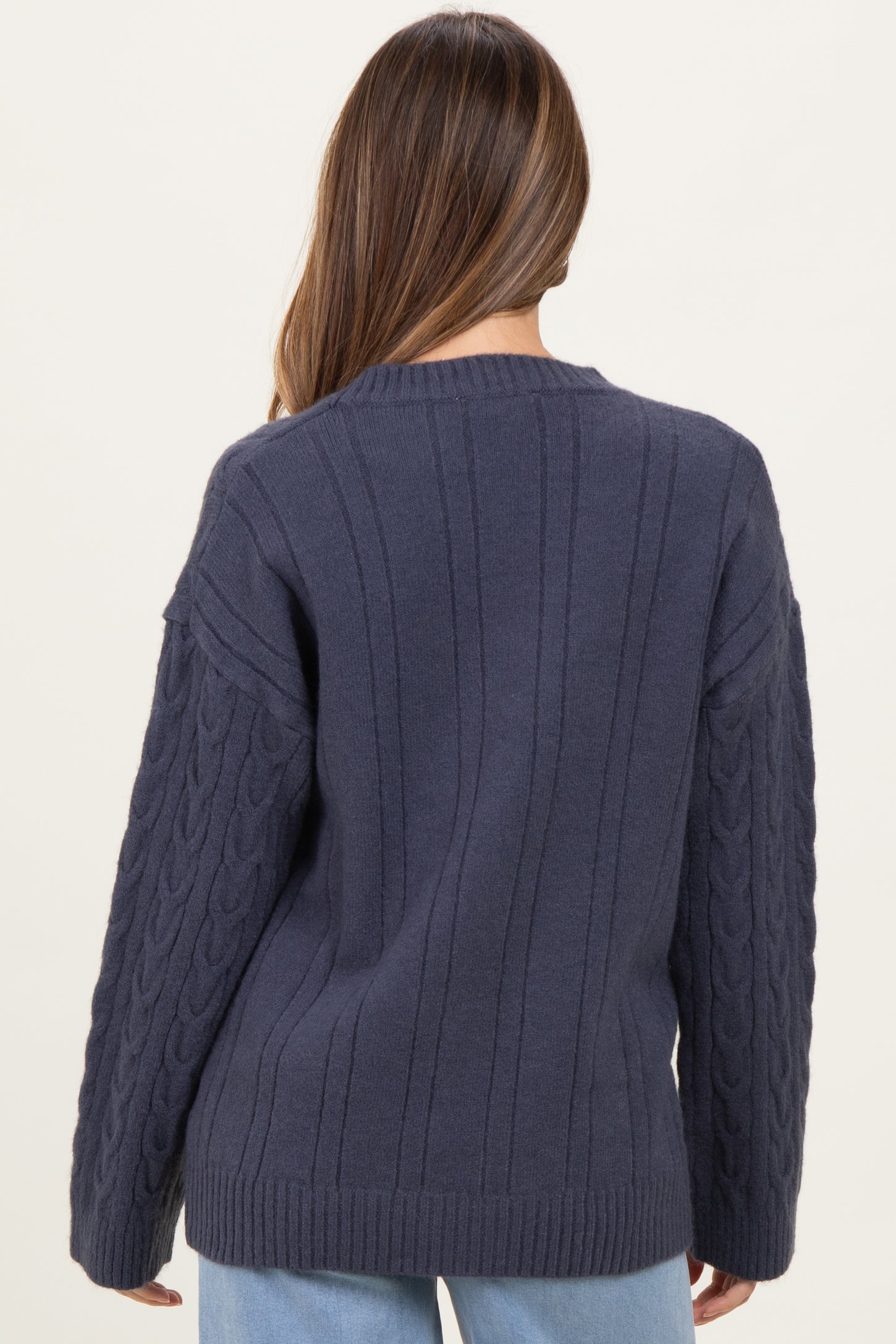 woman wearing a dark blue maternity sweater with cable-knit details and a relaxed fit, viewed from the back