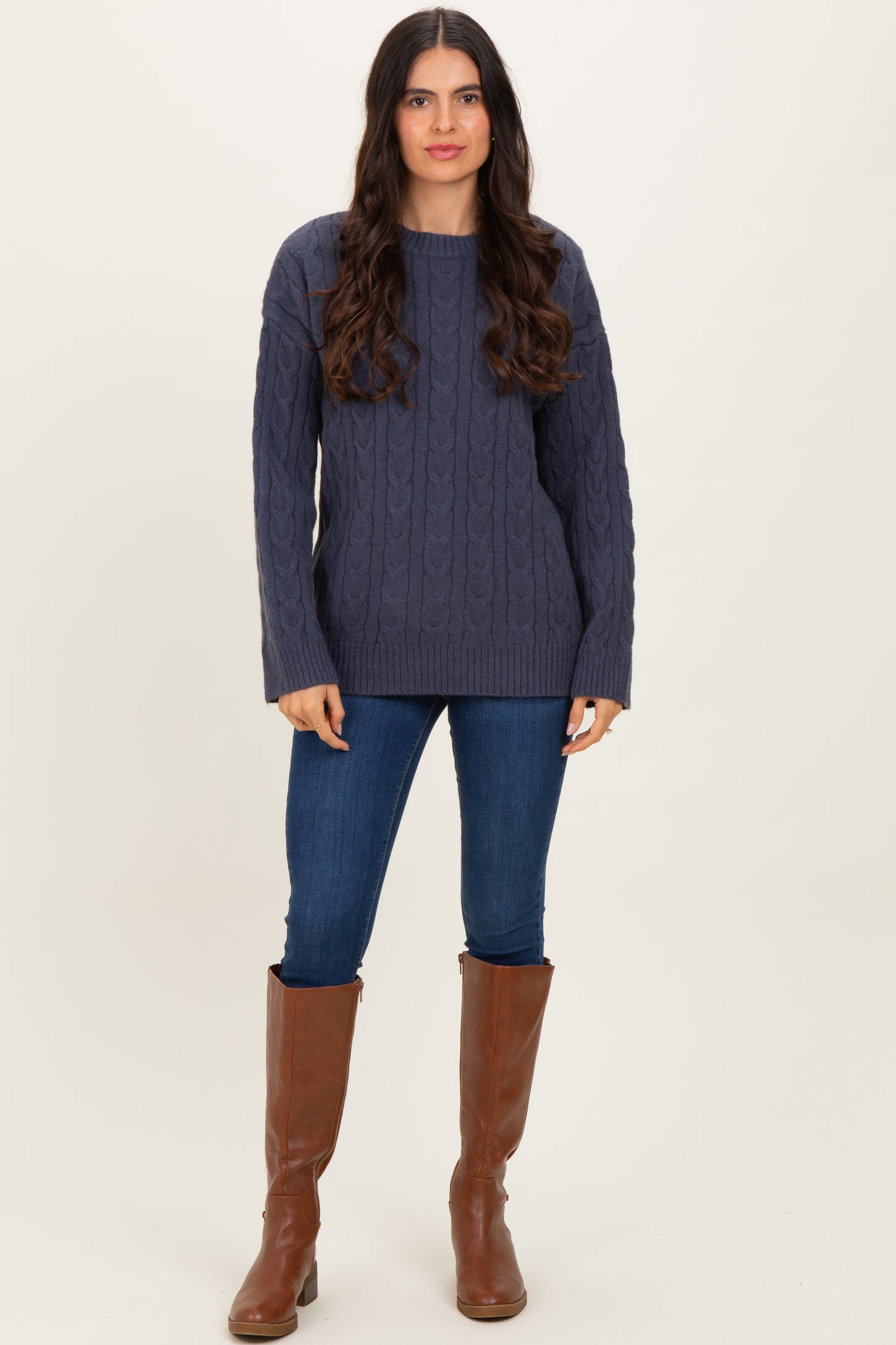 woman wearing a navy blue cable knit sweater with long sleeves, paired with fitted jeans and knee-high brown boots