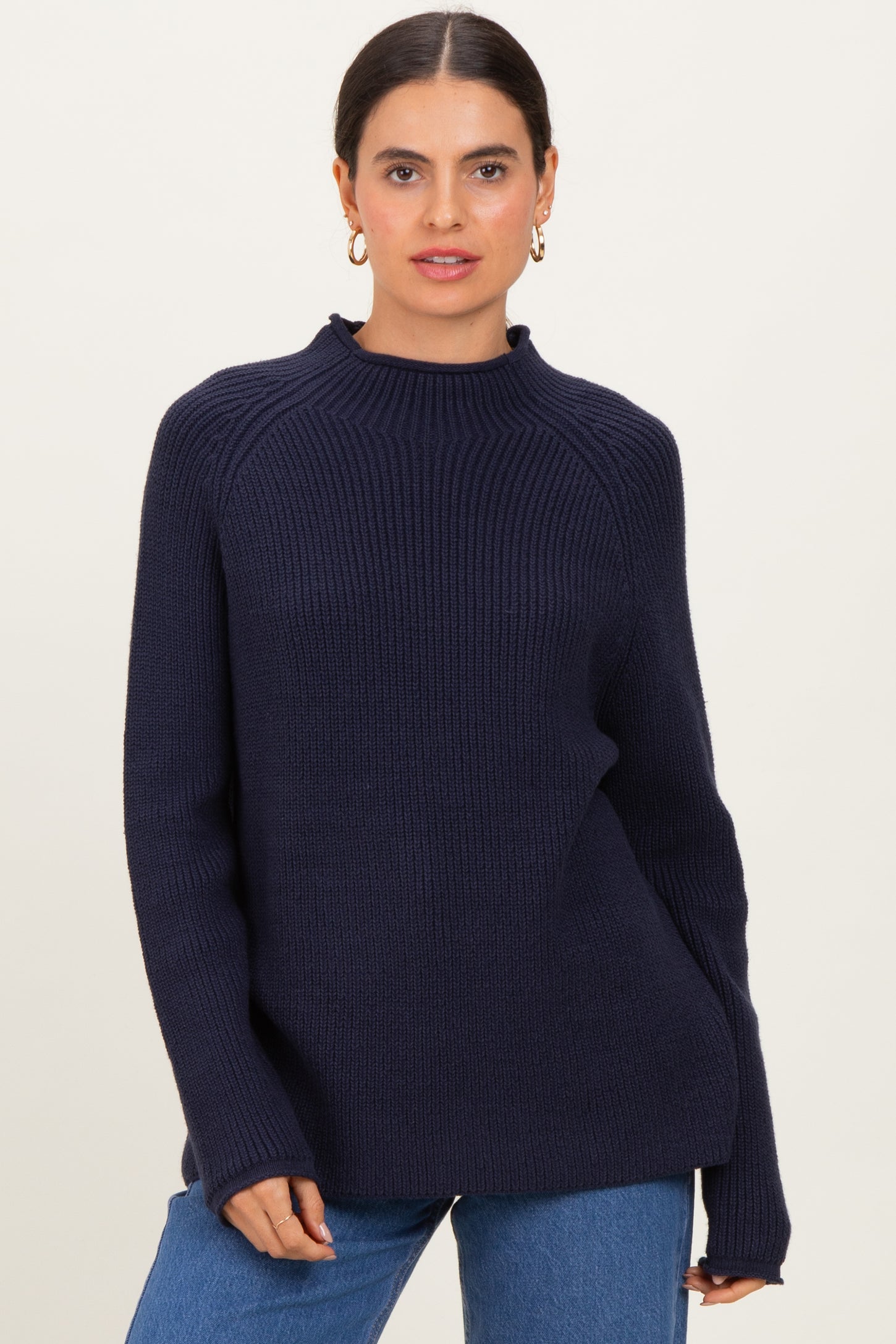 woman wearing a dark navy ribbed knit sweater with a high neckline and relaxed fit, paired with blue jeans