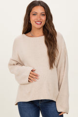 woman wearing a beige oversized maternity sweater and holding her baby bump