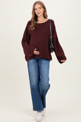 woman wearing a maroon oversized maternity sweater and blue wide-leg jeans, holding her baby bump