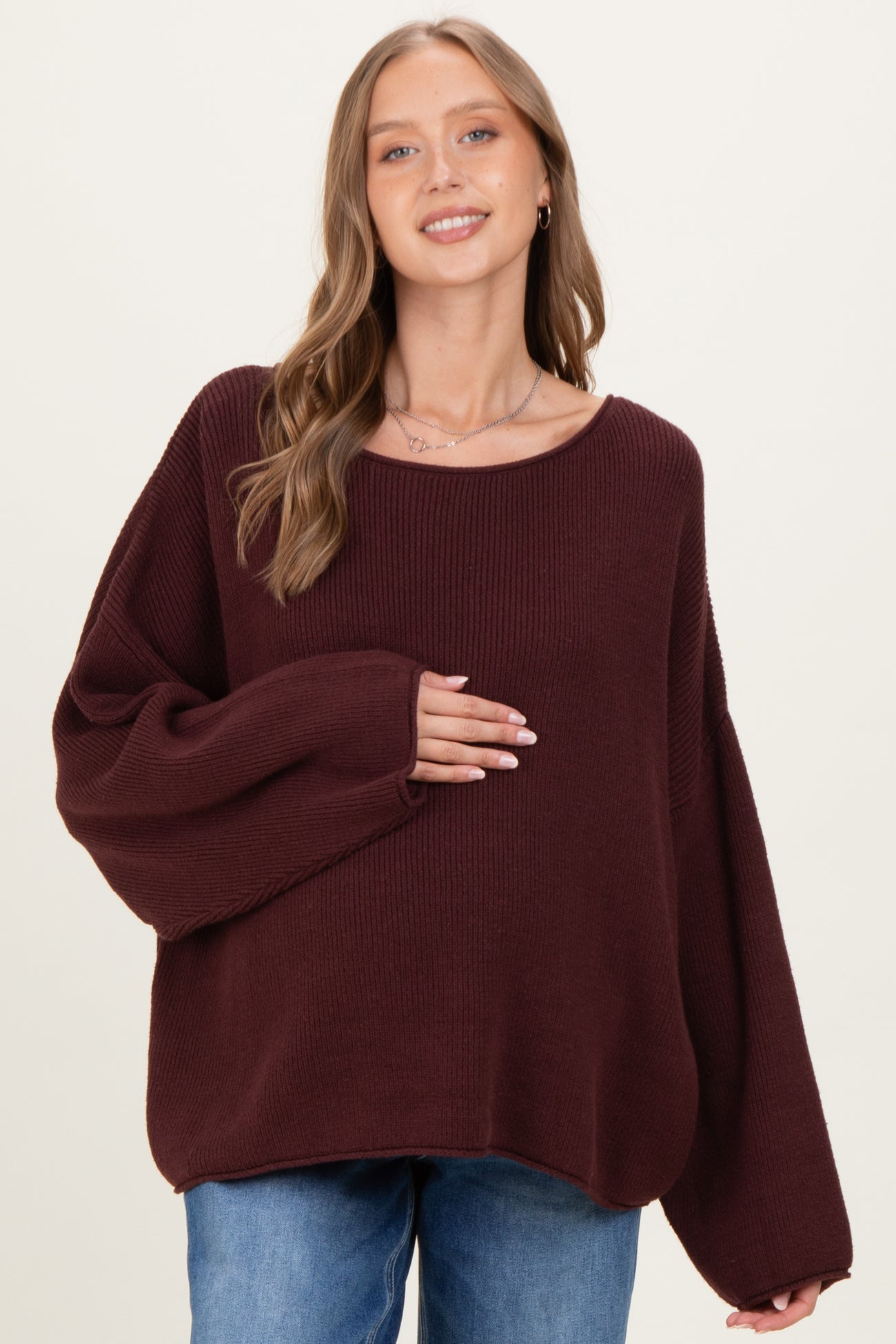 woman wearing a burgundy oversized maternity sweater and gently holding her baby bump