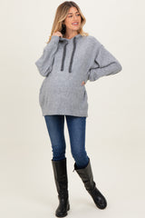 woman wearing a gray cozy maternity hoodie with a drawstring and pocket, paired with blue skinny jeans and black knee-high boots