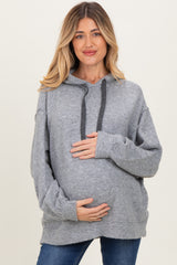 woman wearing a light grey oversized maternity hoodie, holding her baby bump with a smile