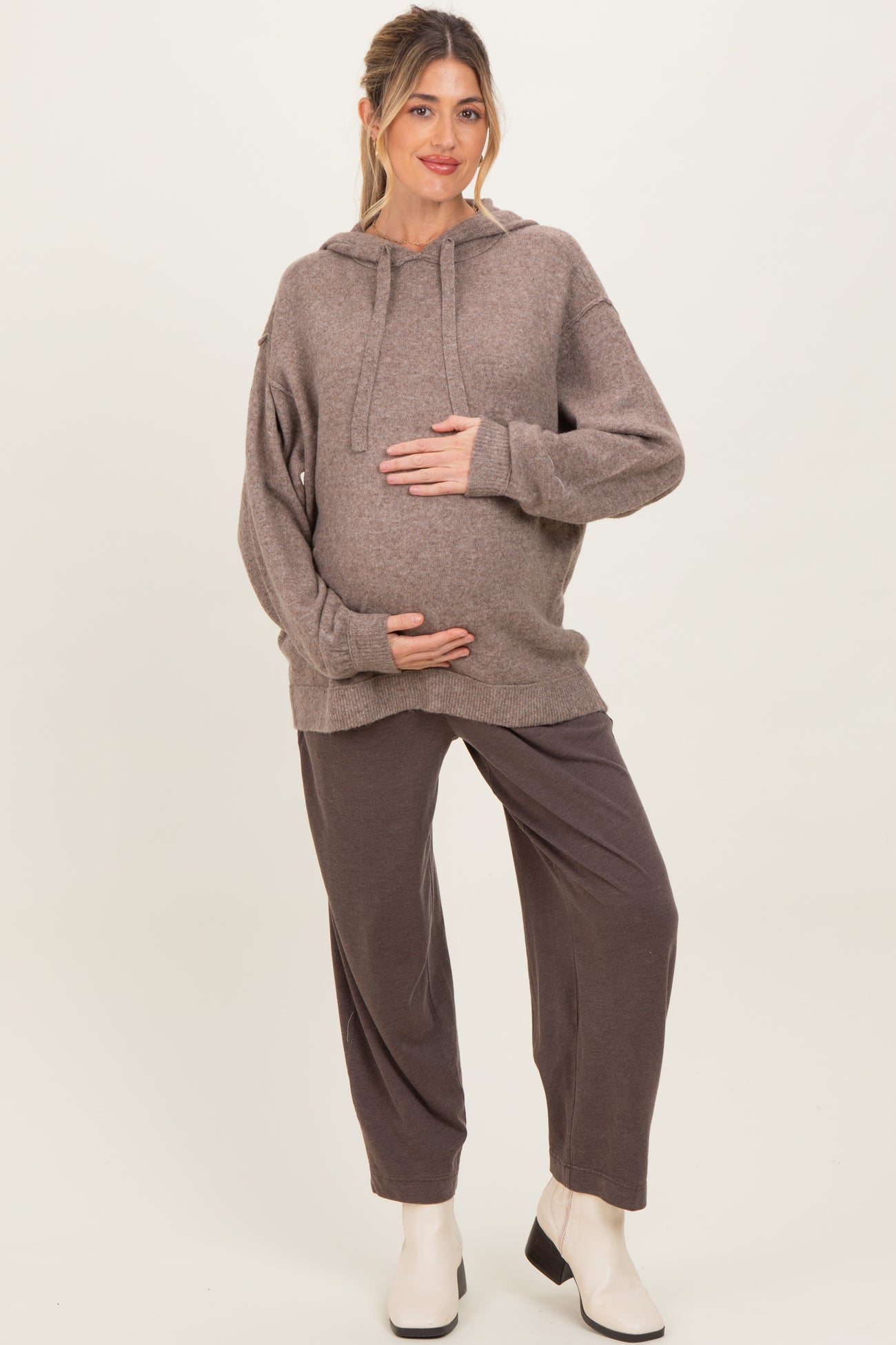woman wearing a brown maternity hoodie and matching sweatpants, holding her baby bump