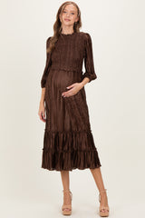 woman wearing a brown pleated maternity dress with smocked bodice and ruffled hem, cradling her baby bump