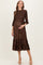 woman wearing a brown pleated maternity dress with smocked bodice and ruffled hem, cradling her baby bump