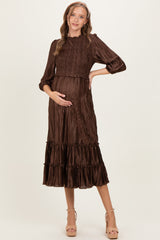 woman wearing a brown pleated maternity dress with three-quarter sleeves and a tiered skirt, showing her baby bump
