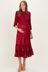 woman wearing a red pleated maternity dress with three-quarter sleeves and tiered skirt, cradling her baby bump