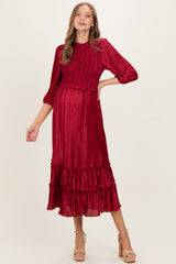 woman wearing a red pleated maternity dress with three-quarter sleeves and ruffle details, showing her baby bump