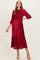 woman wearing a red pleated maternity dress with three-quarter sleeves and ruffle details, showing her baby bump