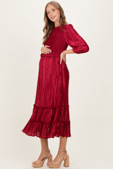 woman wearing a red pleated maternity dress with ruffle details and holding her baby bump