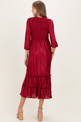 woman wearing a burgundy pleated maternity dress with three-quarter sleeves and a ruffled hemline