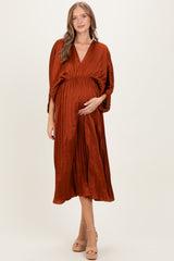 woman wearing a rust-colored maternity dress with a pleated skirt and v-neckline, holding her baby bump