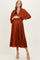 woman wearing a rust-colored pleated maternity dress with a deep v-neck and a baby bump visible