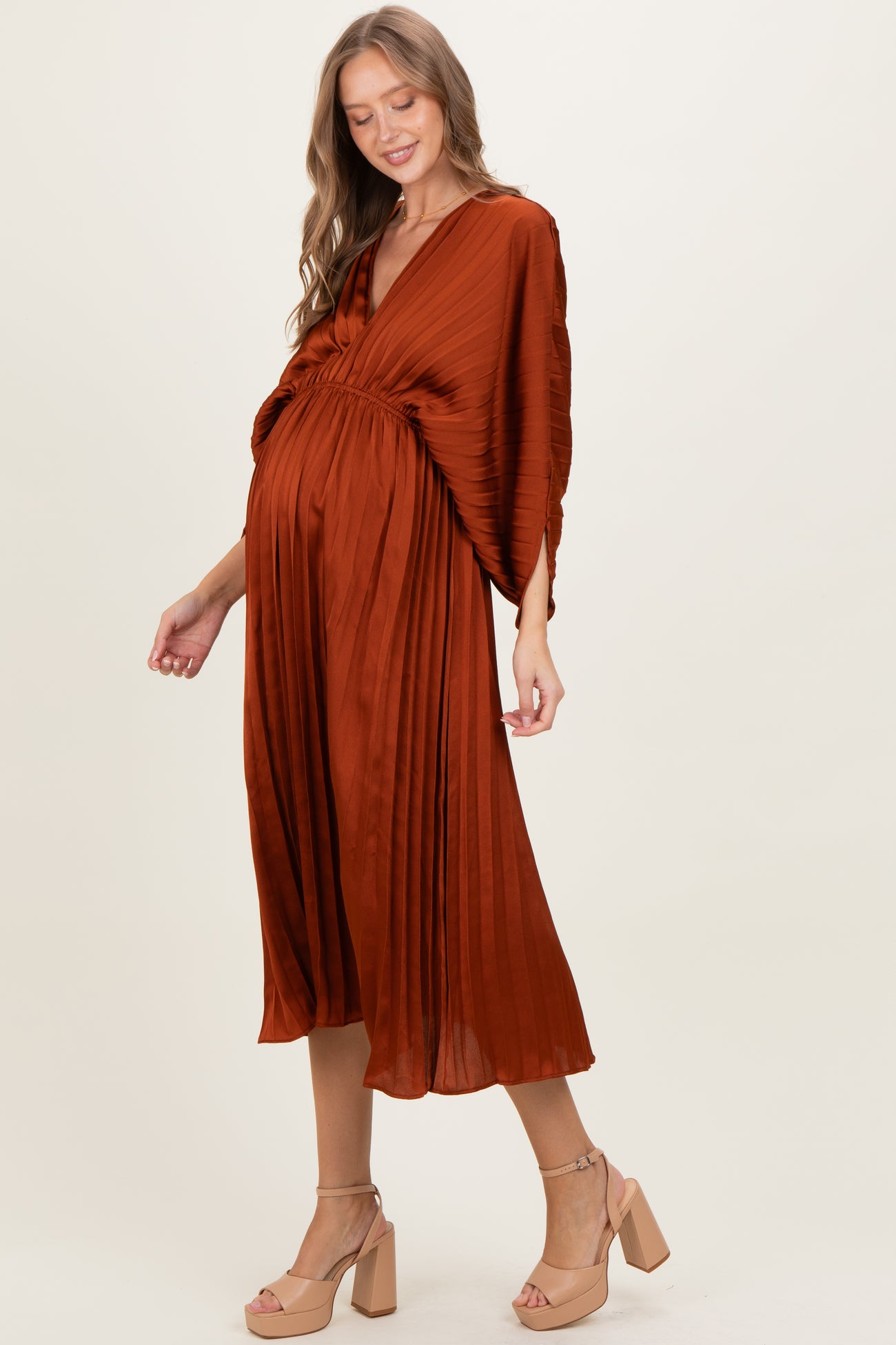 woman wearing an earthy orange pleated maternity dress with a v-neck and flowing sleeves, showing her baby bump