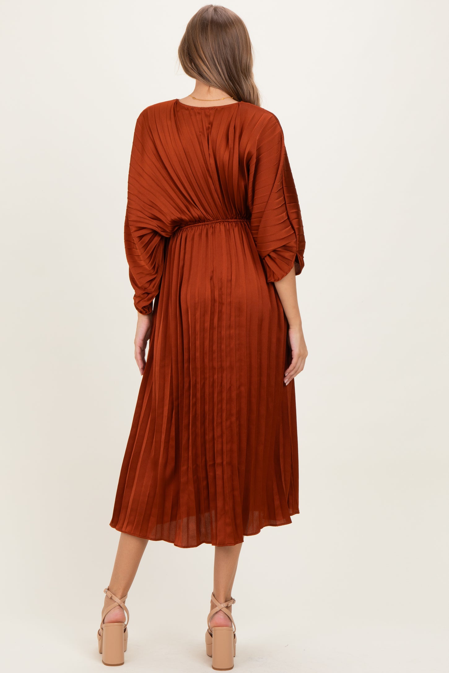 woman wearing a rust pleated maternity dress with a cinched waist and balloon sleeves, shown from the back