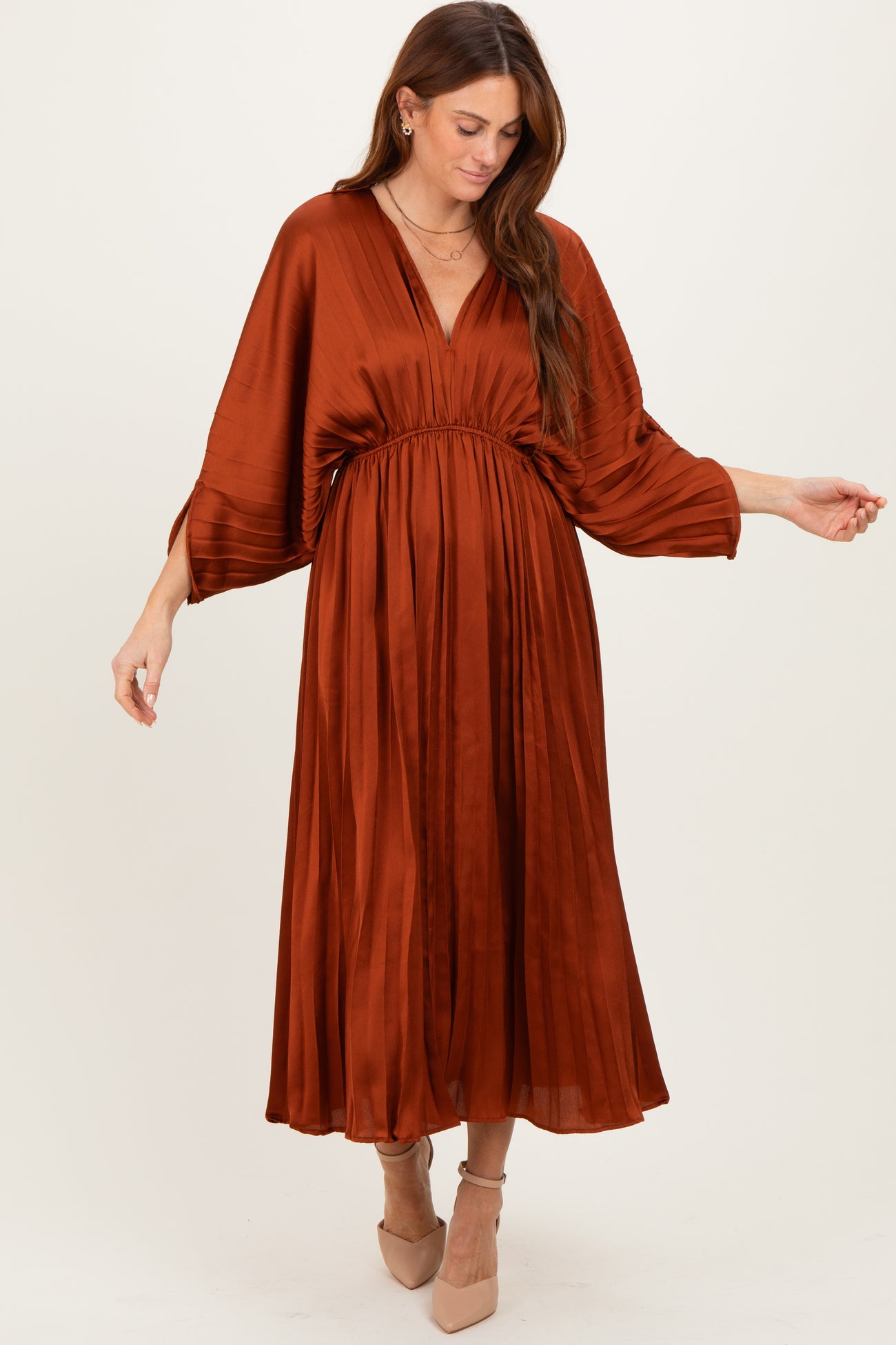 woman wearing a rust orange pleated maxi dress with a cinched waist and bell sleeves