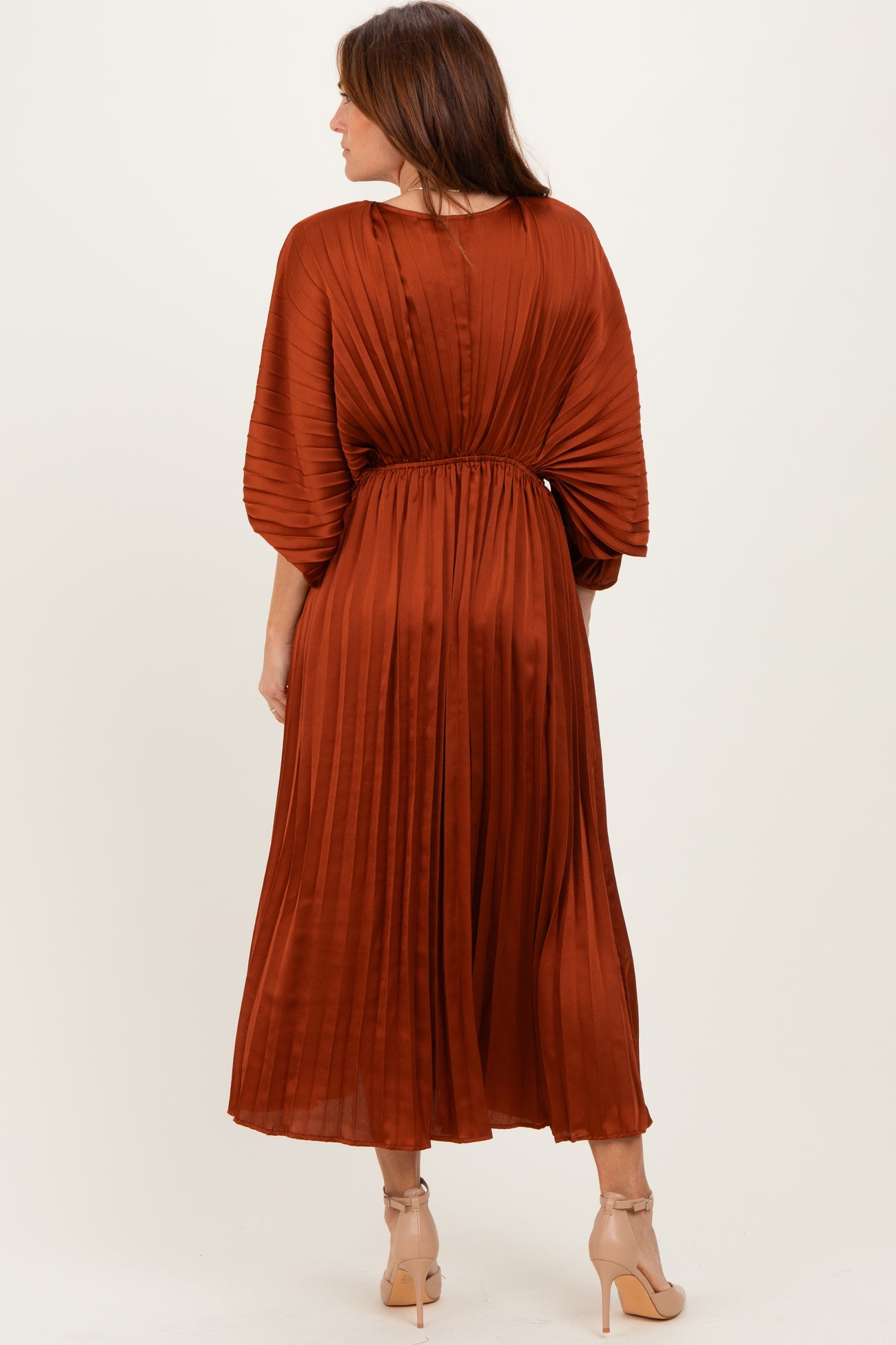 woman wearing a rust-colored pleated midi dress with a cinched waist and balloon sleeves, showing the back view