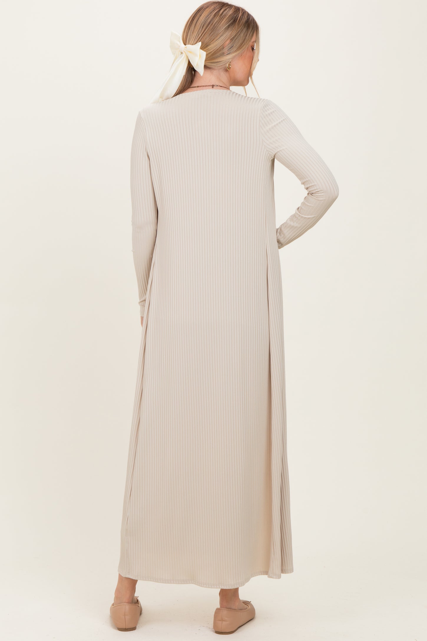 woman wearing a long beige ribbed dress with long sleeves, shown from the back