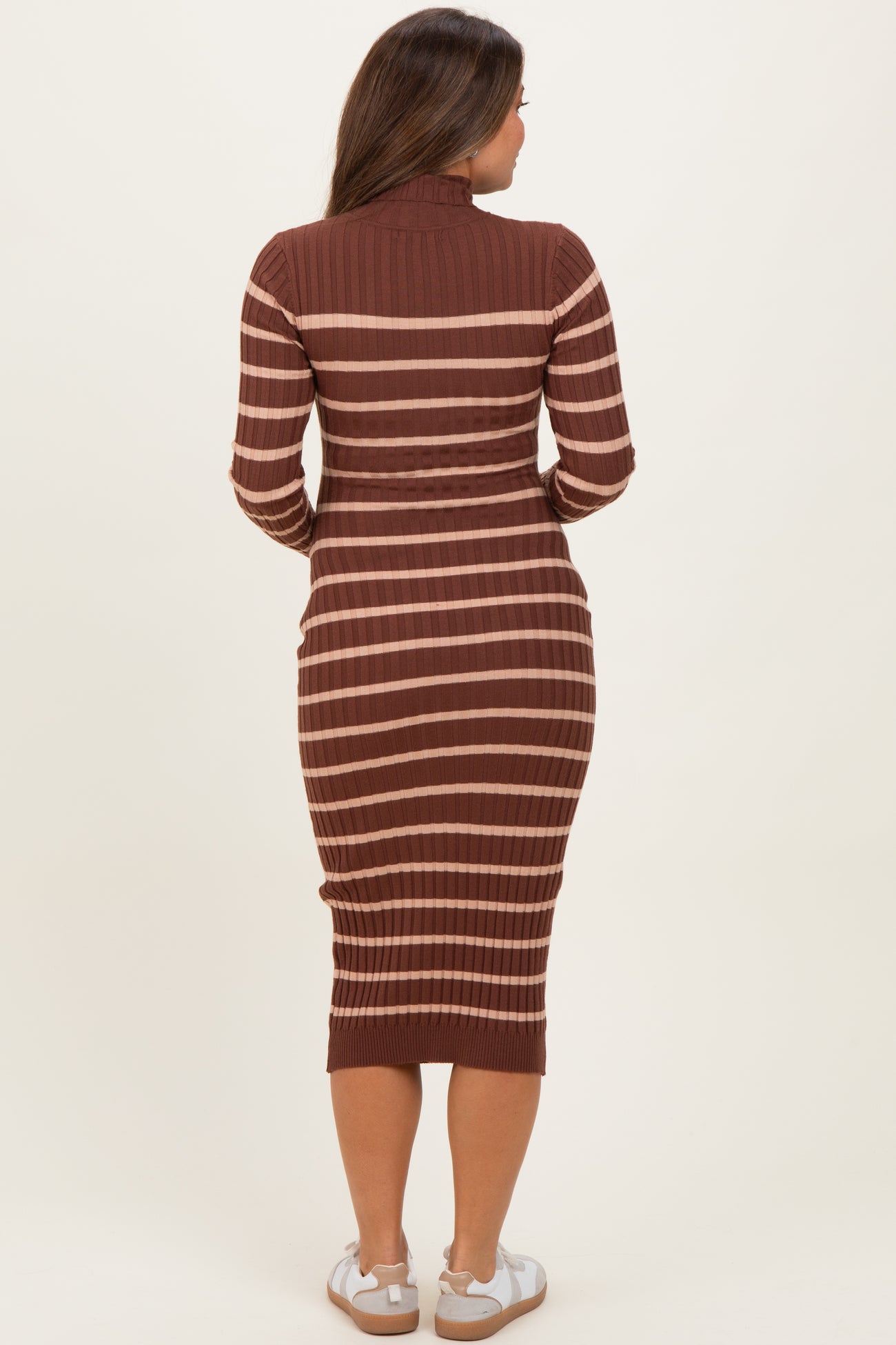 woman wearing a rust and beige striped maternity dress with a fitted silhouette and long sleeves, showing a baby bump