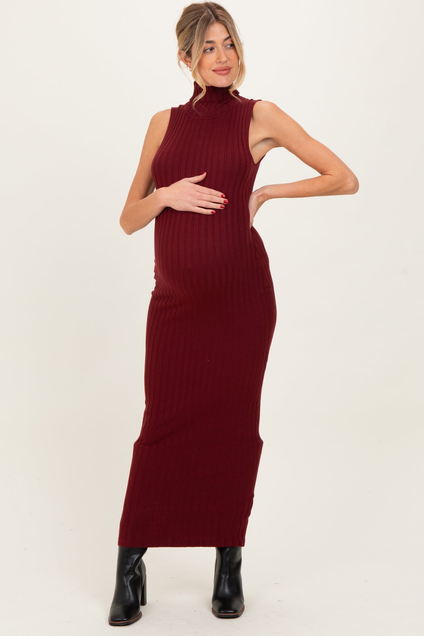 woman wearing a burgundy ribbed maternity dress, showing off her baby bump, styled with black ankle boots