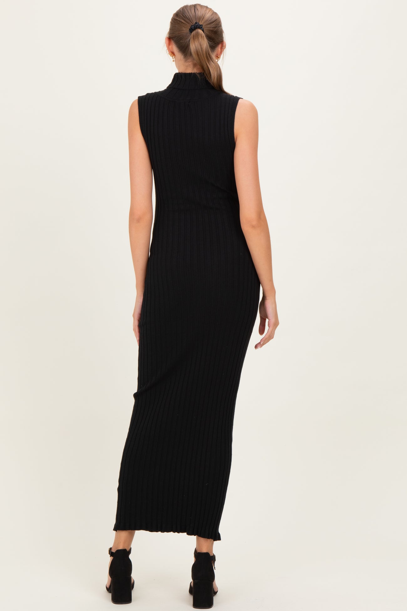 woman wearing a fitted black ribbed maternity dress with a sleeveless design and a long silhouette, side slit visible