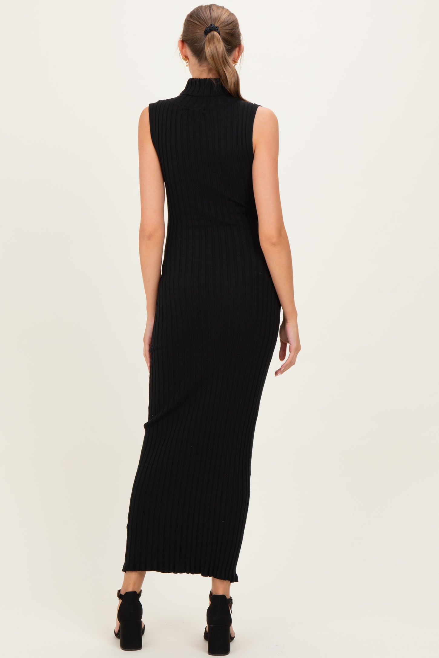 woman wearing a fitted black ribbed maternity dress with a sleeveless design and a long silhouette, side slit visible