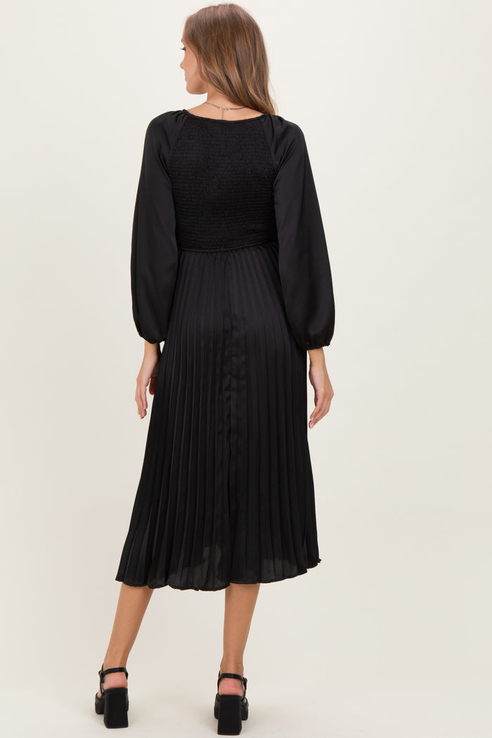 woman wearing a black pleated maternity dress with long sleeves and a smocked bodice, showing the back view
