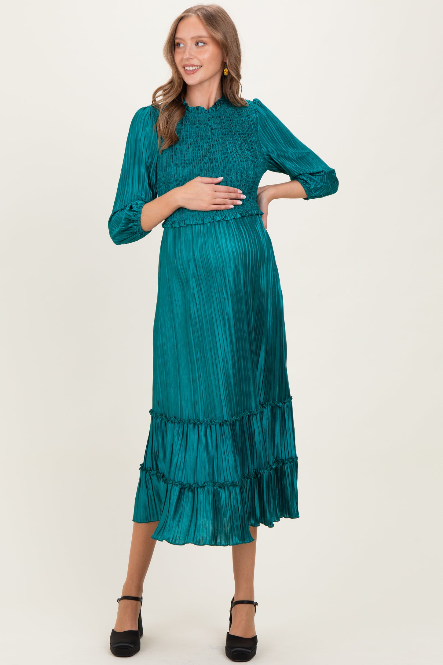 woman wearing a teal maternity dress with smocked bodice and tiered skirt, holding her baby bump