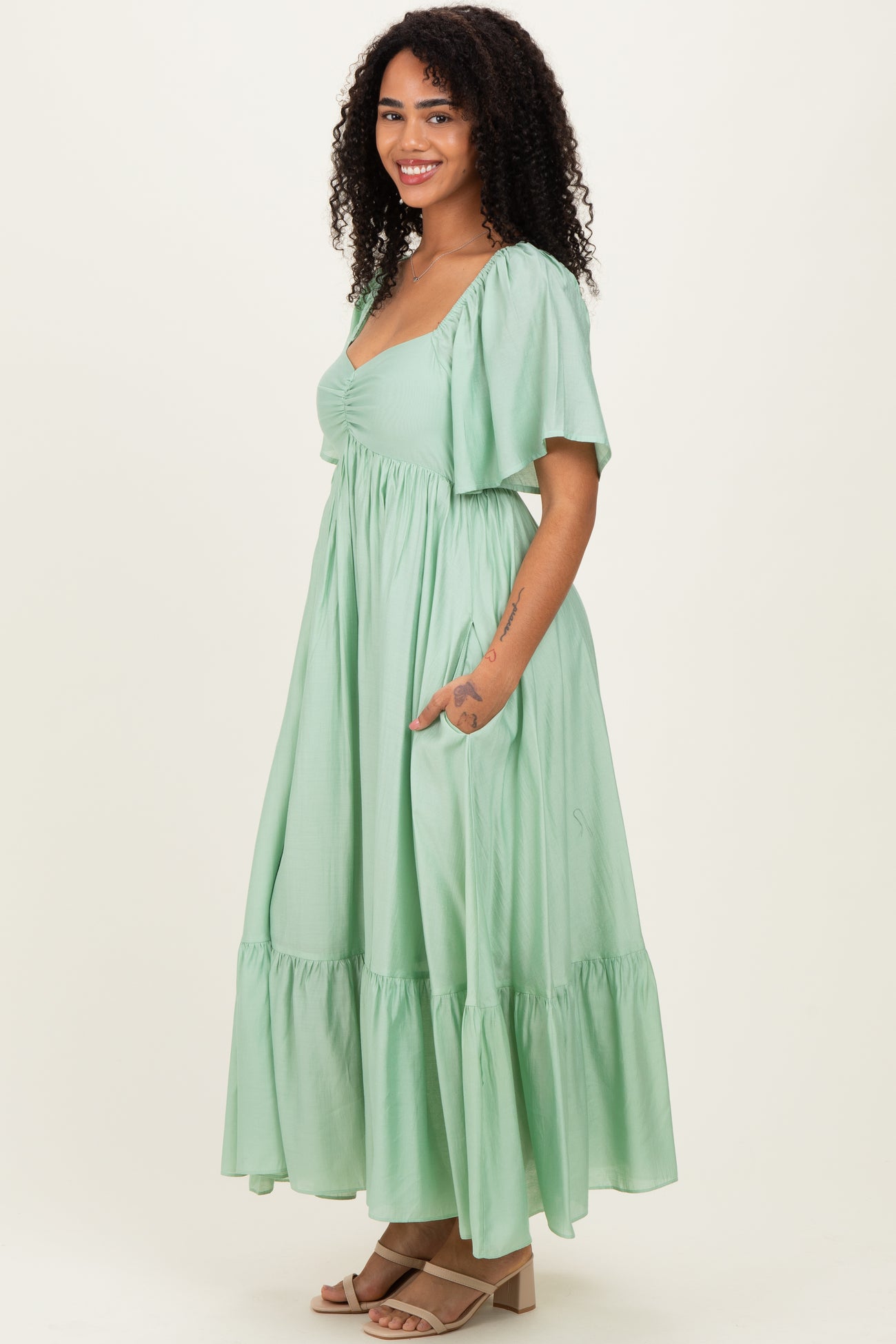 woman wearing a light green maxi dress with short sleeves and a ruffled hem, posing with hands in pockets
