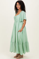 woman wearing a light green maxi dress with short sleeves and a ruffled hem, posing with hands in pockets