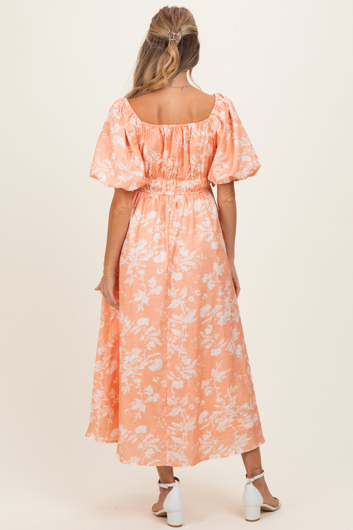 woman wearing a floral patterned orange maternity dress with puff sleeves and a smocked waist, showing her back