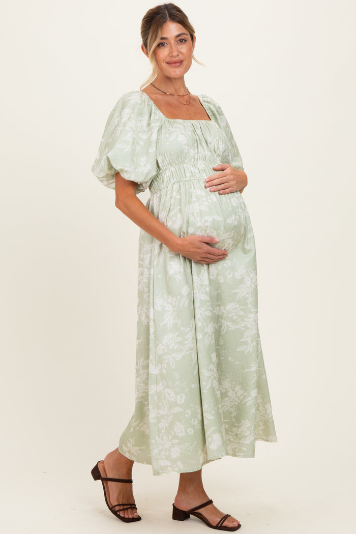 woman wearing a light green floral print maternity dress with puff sleeves and a visible baby bump