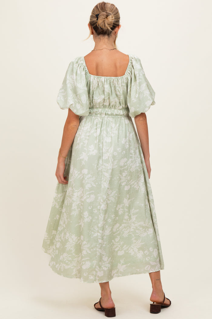 woman wearing a light green floral maternity dress with puff sleeves and a cinched waist, showing an elegant back view