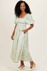 woman wearing a light green floral midi dress with puff sleeves and a cinched waist, standing with one hand in a pocket