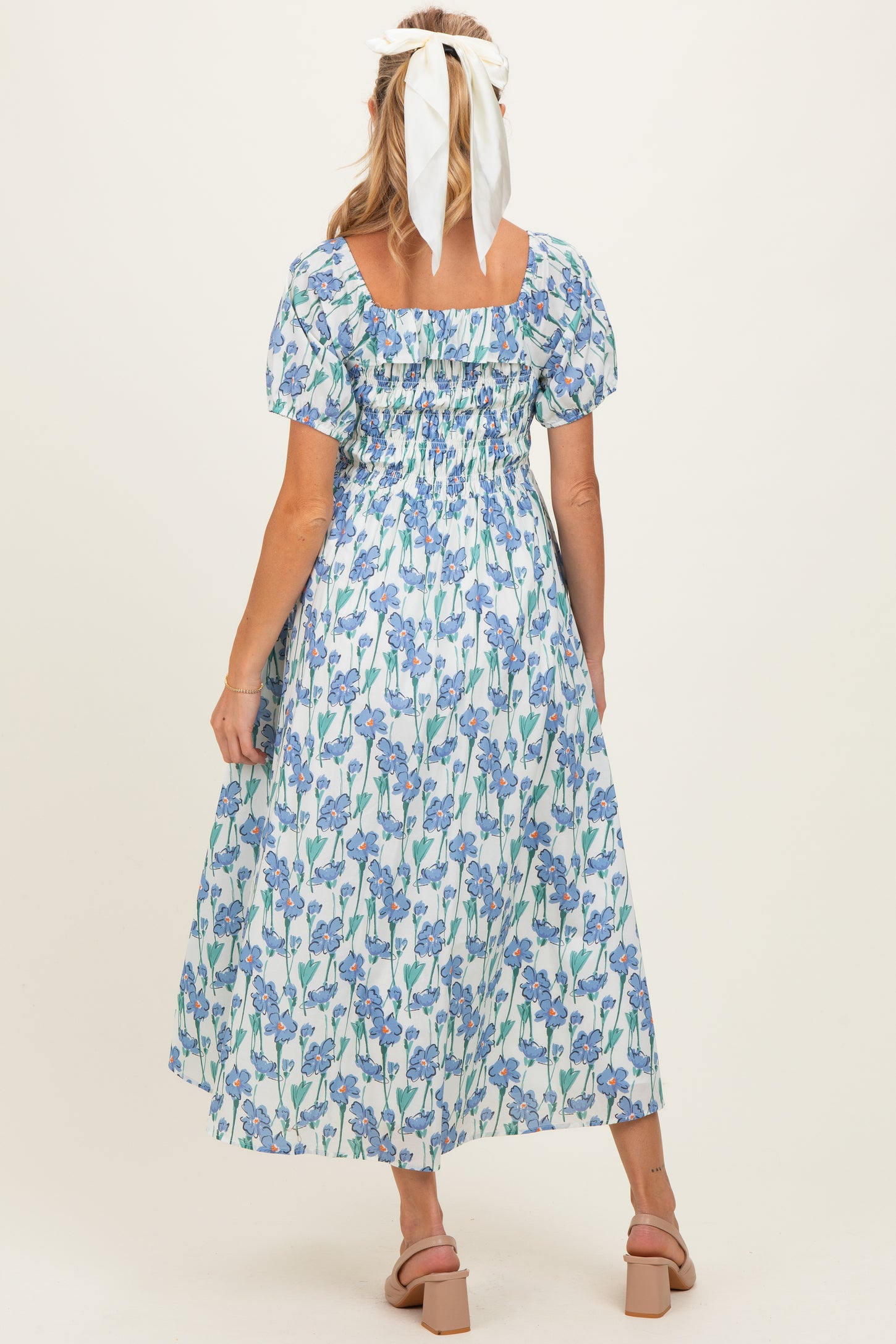 woman wearing a floral maternity dress with puff sleeves and a square neckline, showing her back and long flowy skirt