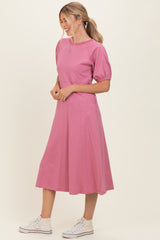 woman wearing a pink puff sleeve midi dress and white sneakers standing against a light background