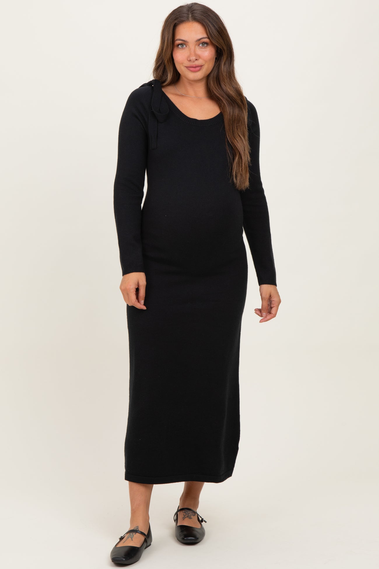 woman wearing a black long sleeve maternity dress with a scoop neckline and side tie detail, showcasing her baby bump